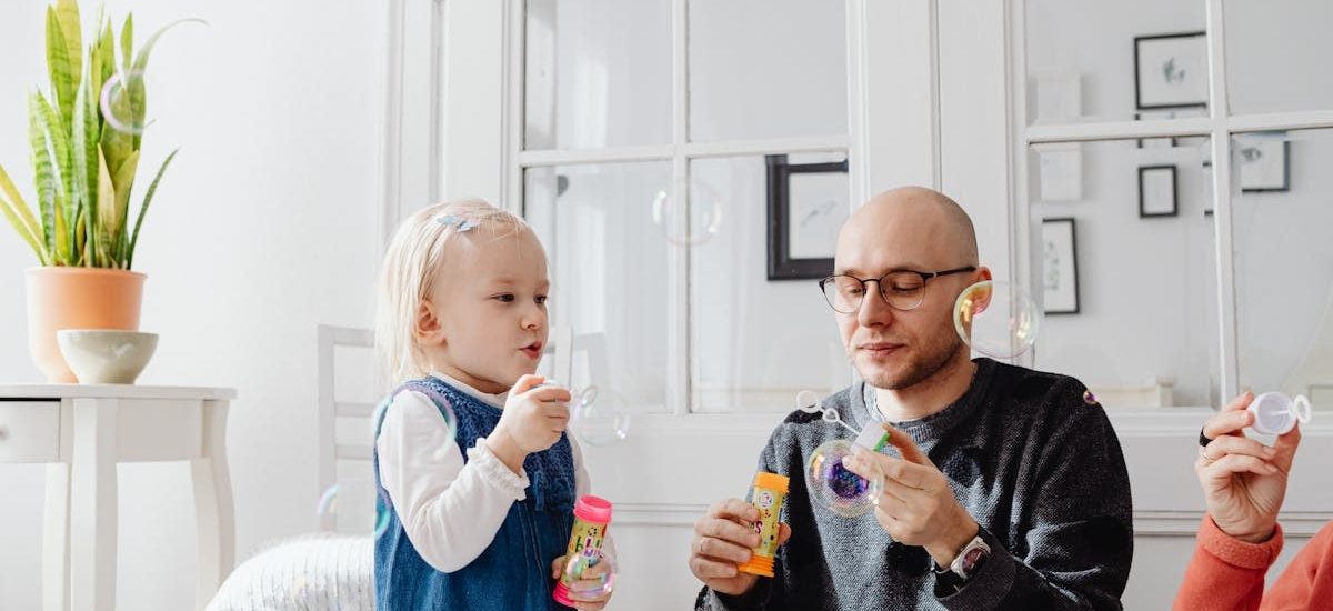 A joyful moment between a father and daughter blowing bubbles indoors, highlighting family fun.